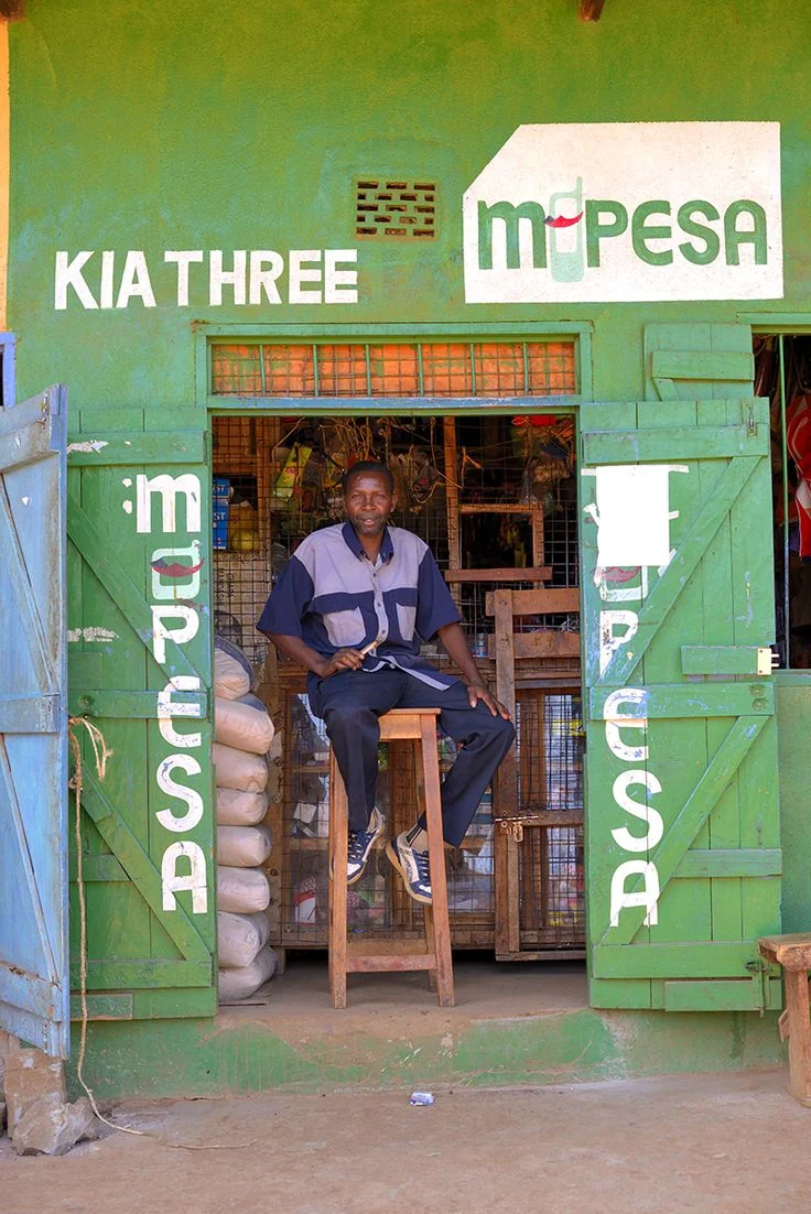 A Kenyan M-Pesa shopfront with a shopkeeper seated at the entrance